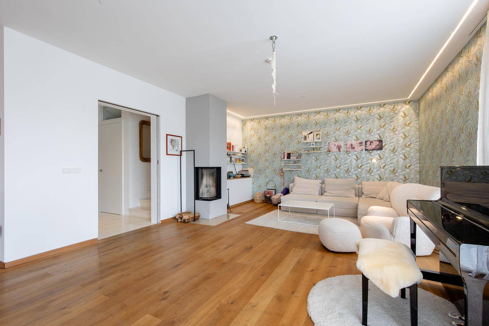 Geräumiges Wohnzimmer mit Holzboden, Kamin und einer eleganten Tapete an der Wand.