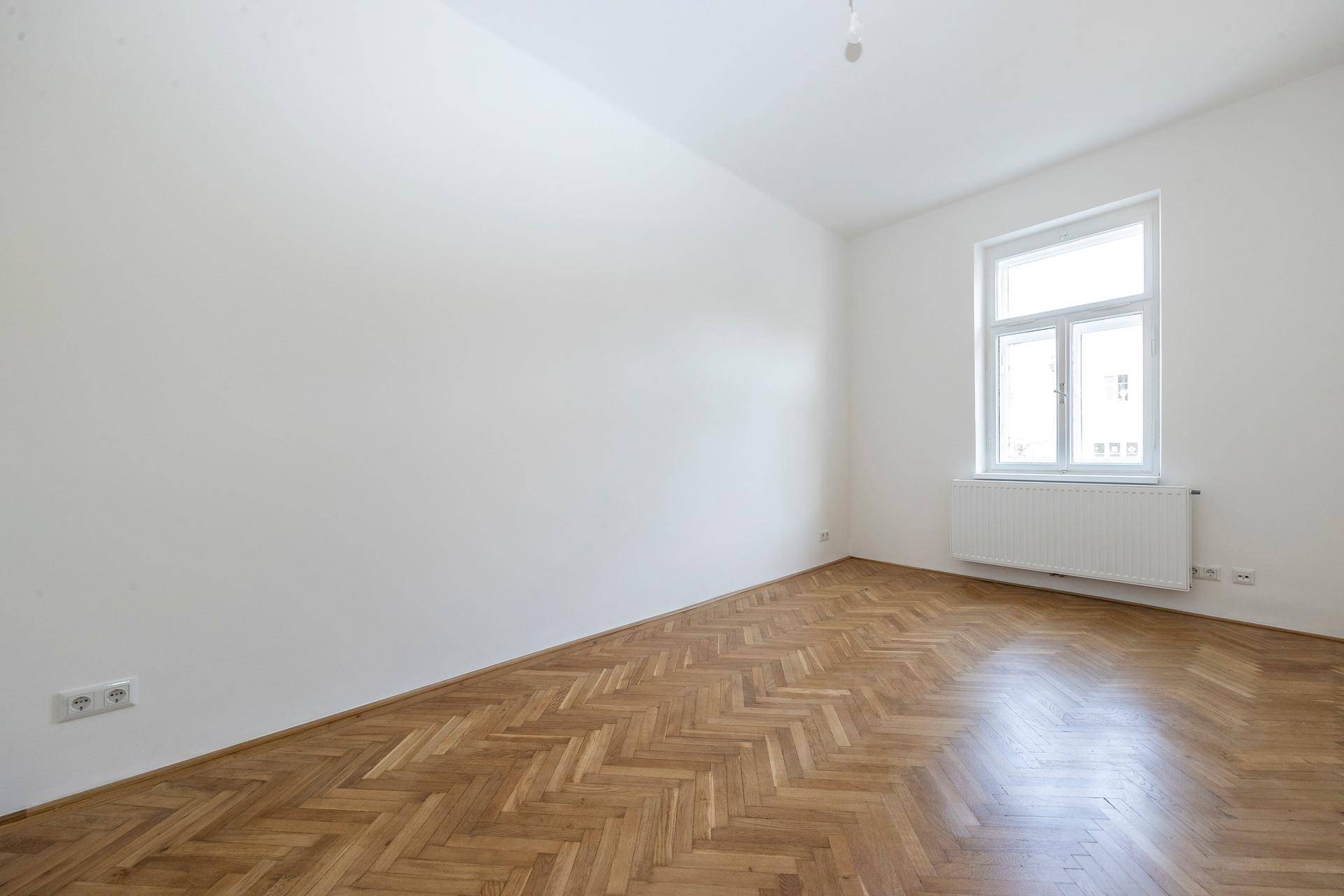 Heller Raum mit schönem Fischgrätparkett und einem Fenster, das für eine angenehme Atmosphäre sorgt.