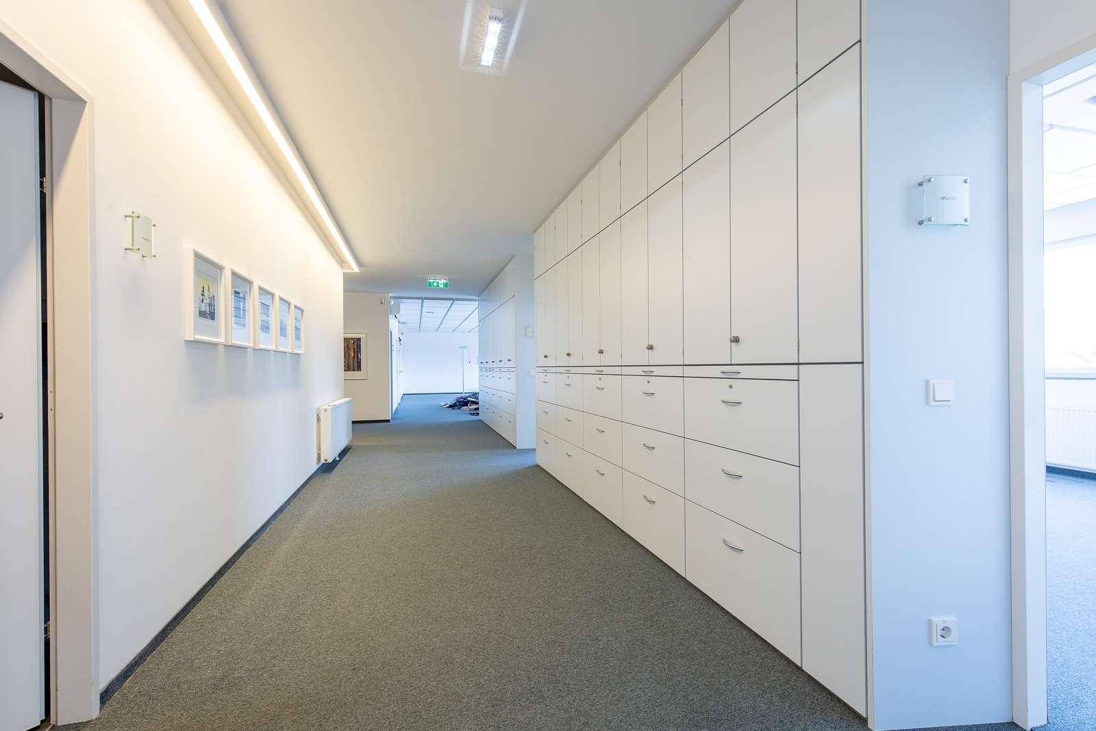 Langer Bürogang mit weißen Einbauschränken, Teppichboden und heller Beleuchtung.