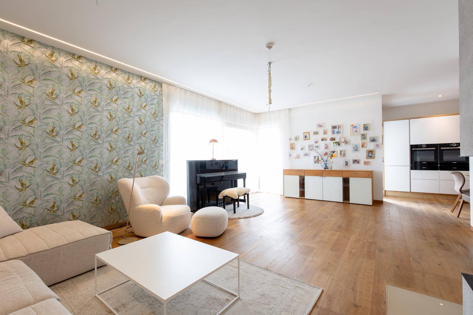 Helles Wohnzimmer mit großen Fenstern, Holzboden und einem Flügel, der zum Entspannen einlädt.