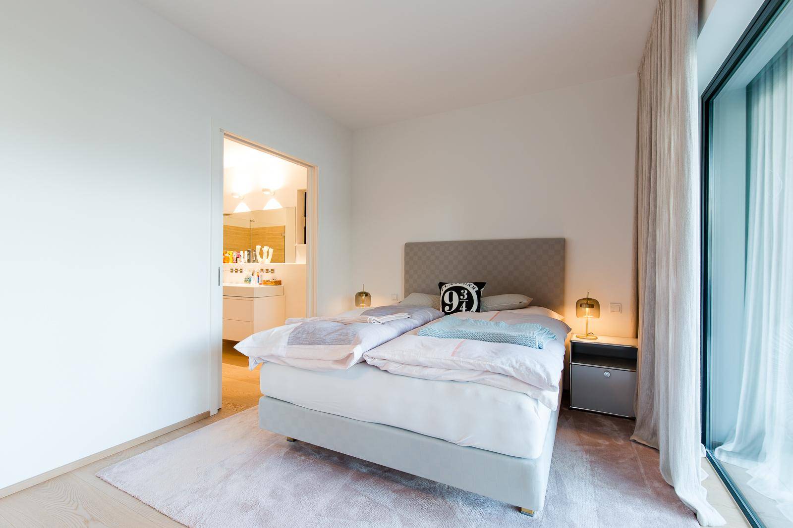 Helles Schlafzimmer mit Doppelbett, Teppichboden und direktem Zugang zum Badezimmer.