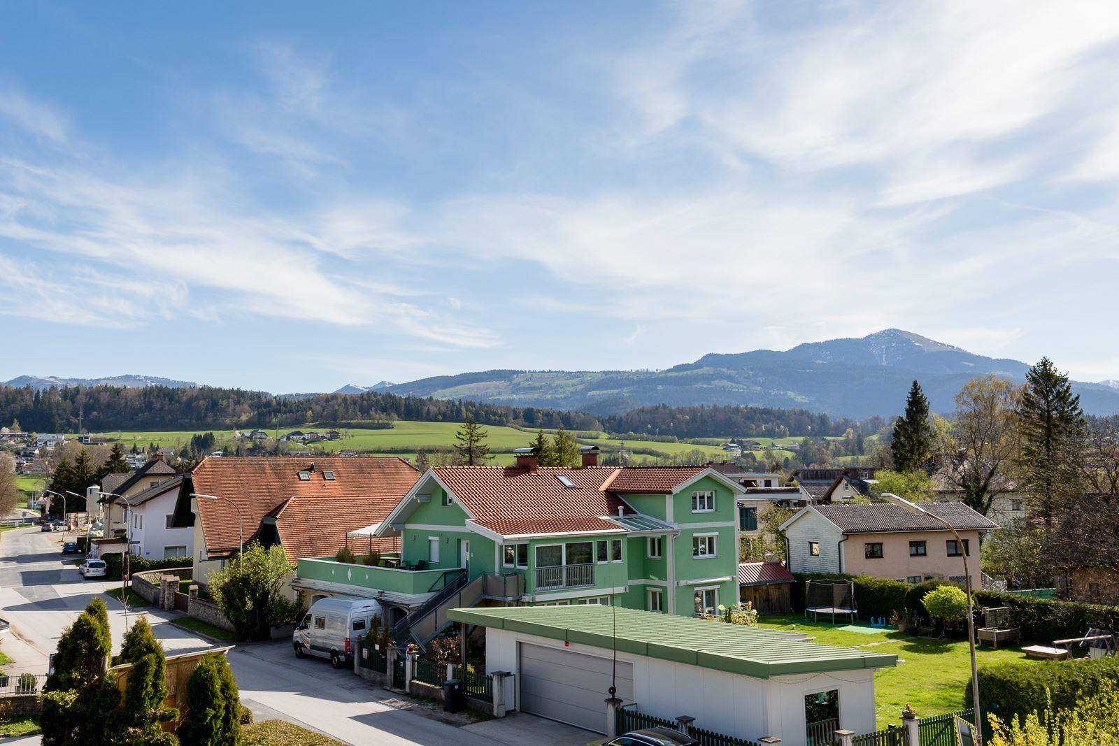 Weitläufiger Blick über eine ländliche Wohngegend mit Bergen im Hintergrund.