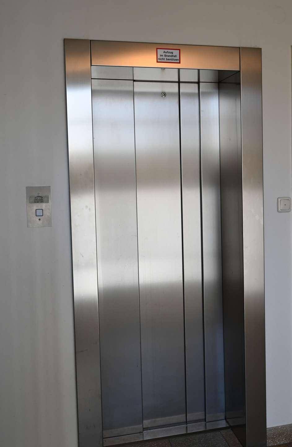 Moderner Aufzug mit Edelstahltüren in einem hellen Flurbereich des Gebäudes.