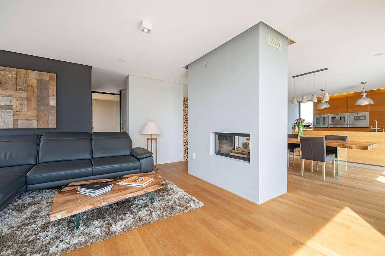 Offener Wohn- und Essbereich mit Kamin, Ledersofa und Blick auf die moderne Holzküche.