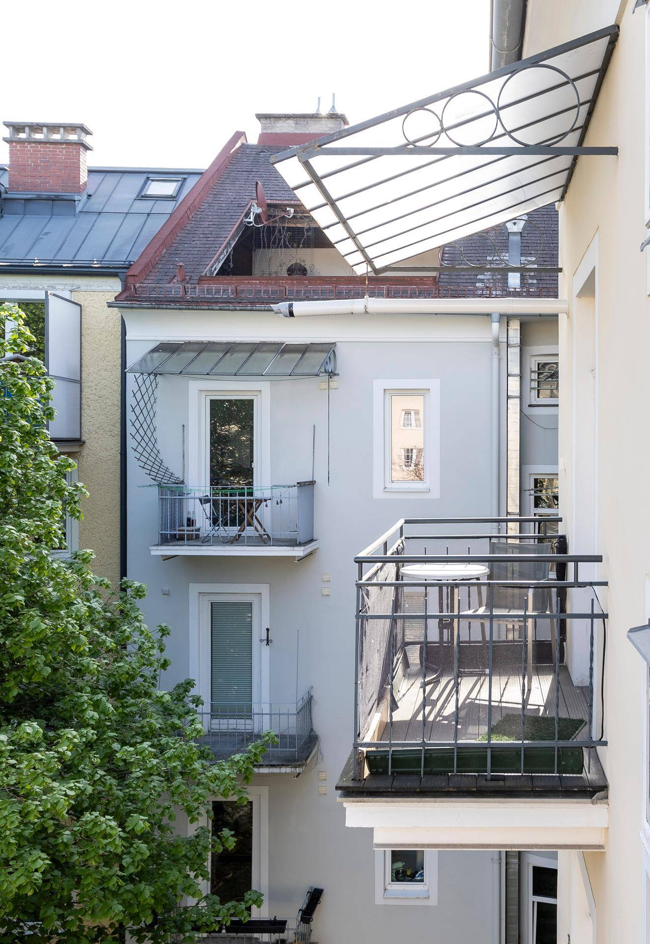 Blick auf die Balkone eines Nachbargebäudes mit schmiedeeisernen Geländern und grünen Bäumen.