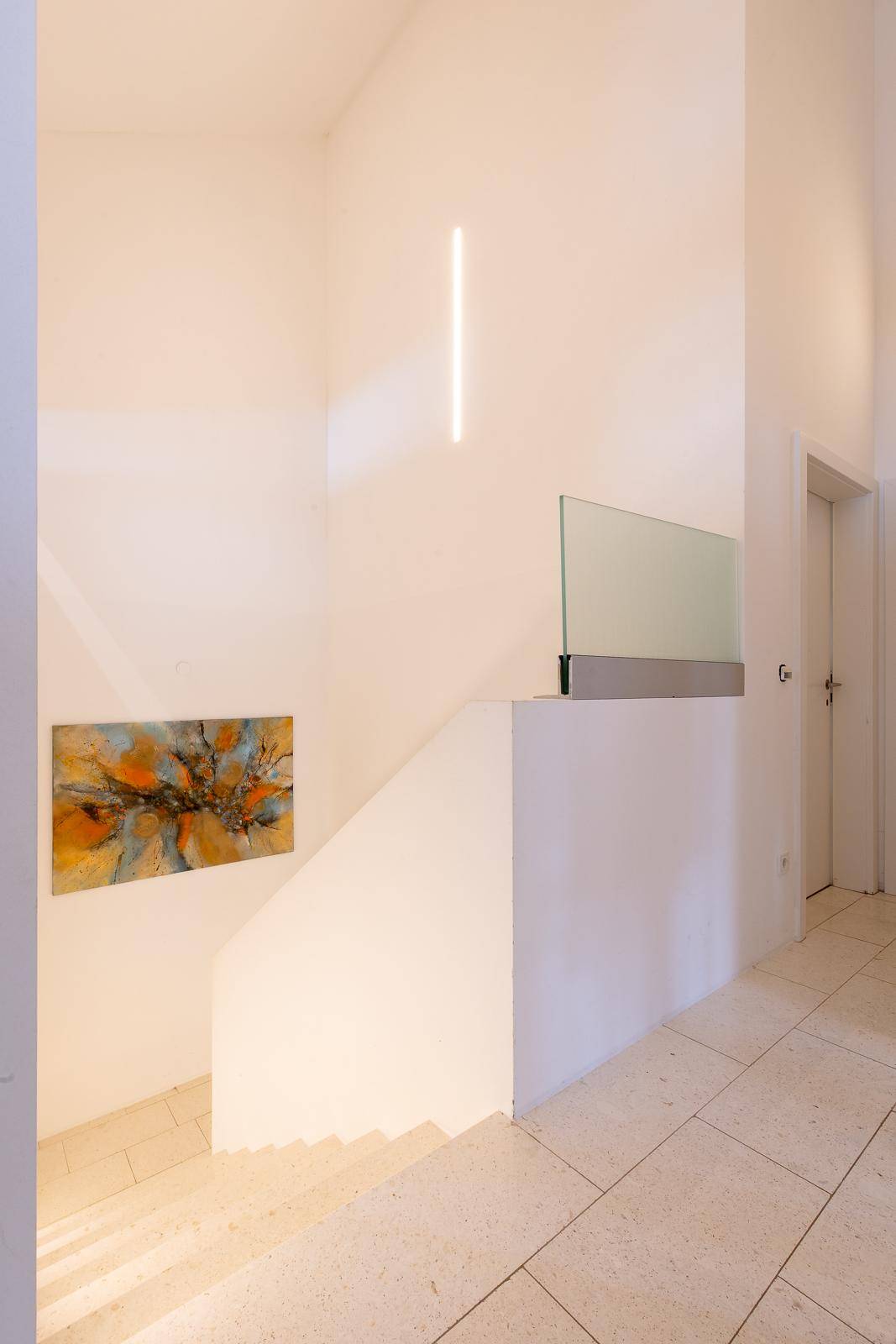 Heller Treppenaufgang mit moderner Beleuchtung und einem Kunstwerk an der Wand.