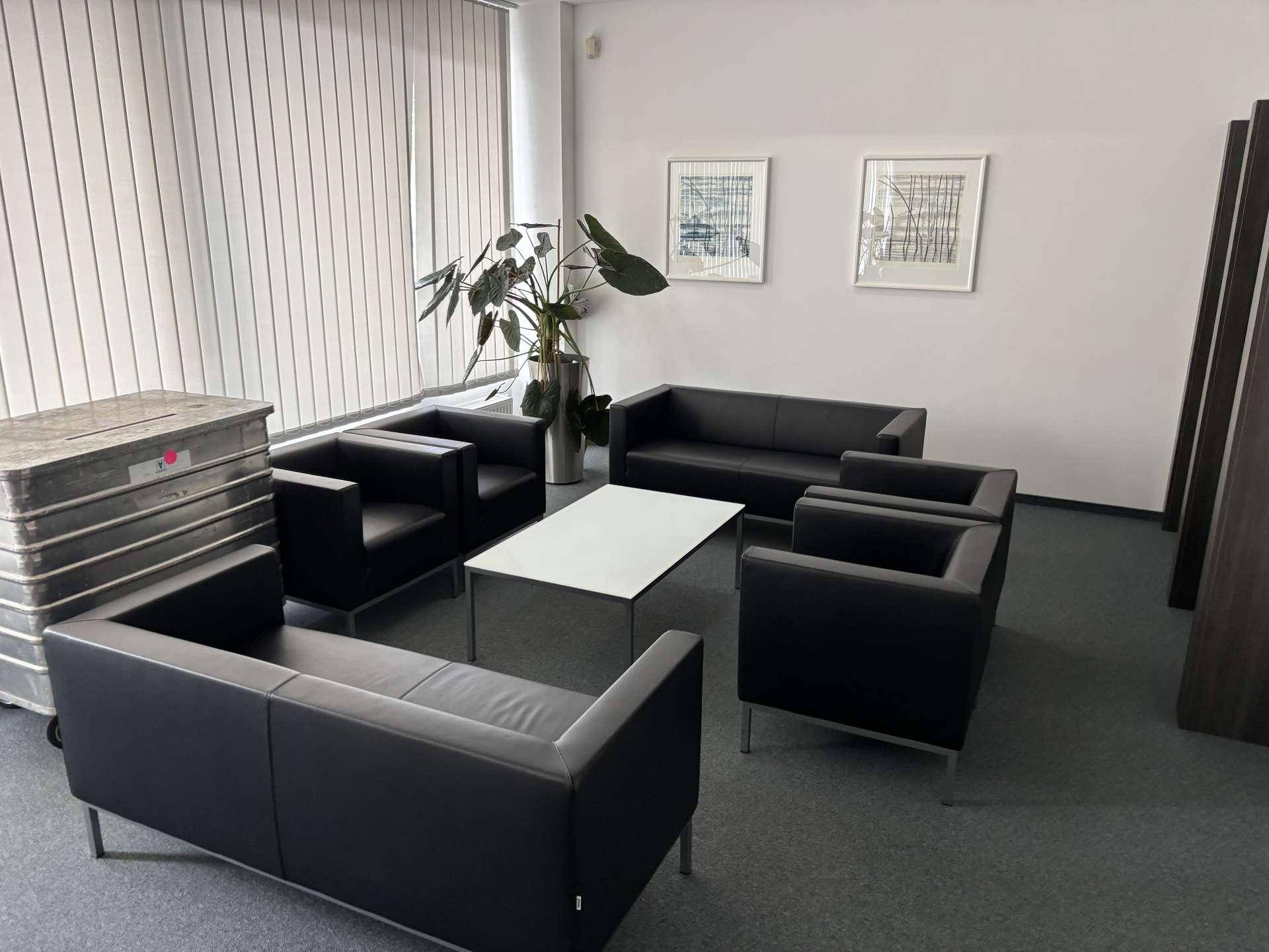 Gemütlicher Loungebereich im Büro mit schwarzen Ledersofas, Sesseln und einem modernen Couchtisch.