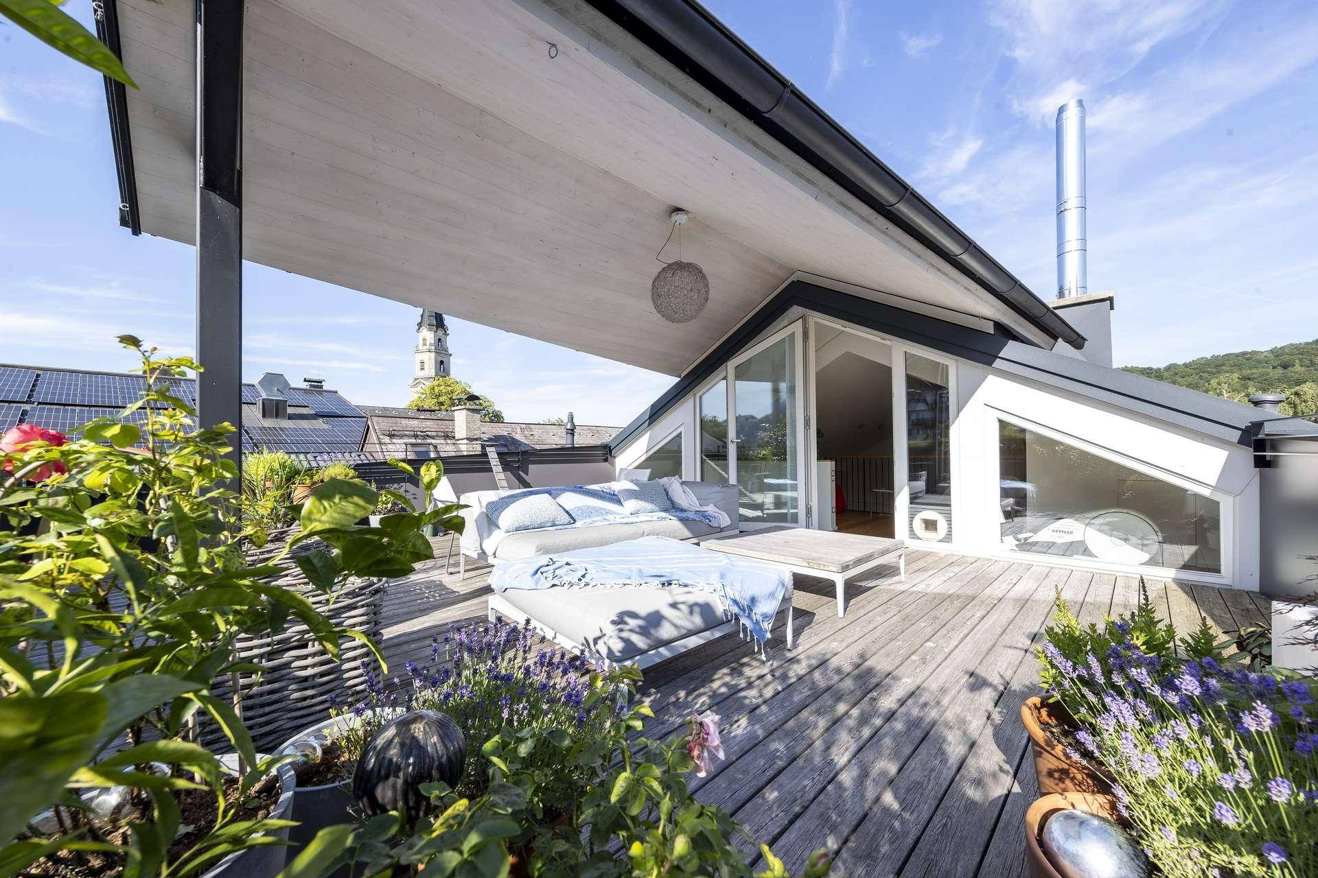 Sonniger Dachterrassenbereich mit Loungemöbeln, Pflanzen und Blick auf einen Kirchturm.