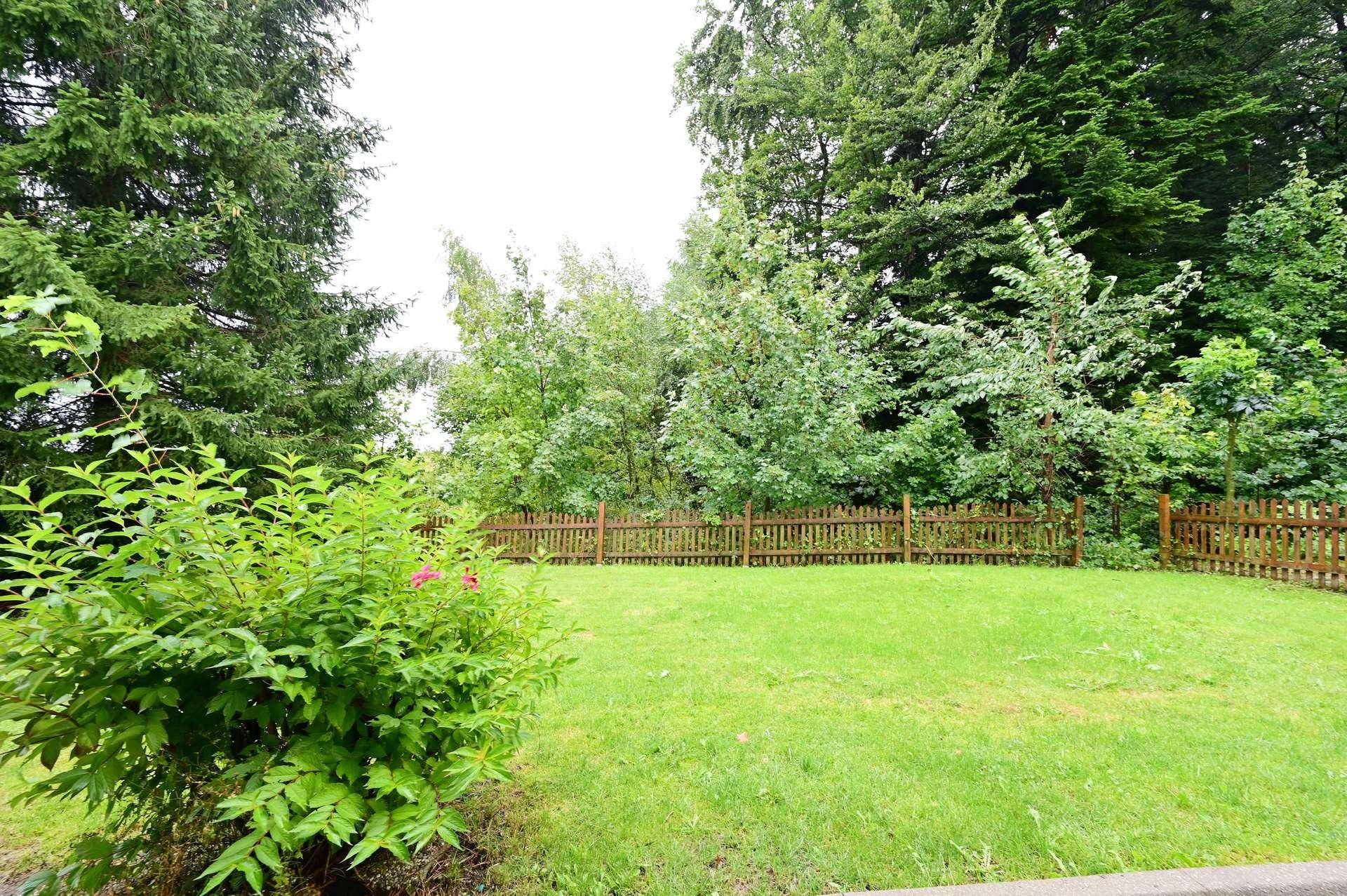 Gepflegter Gartenbereich mit Rasenfläche, Holzzaun und vielfältiger Bepflanzung.