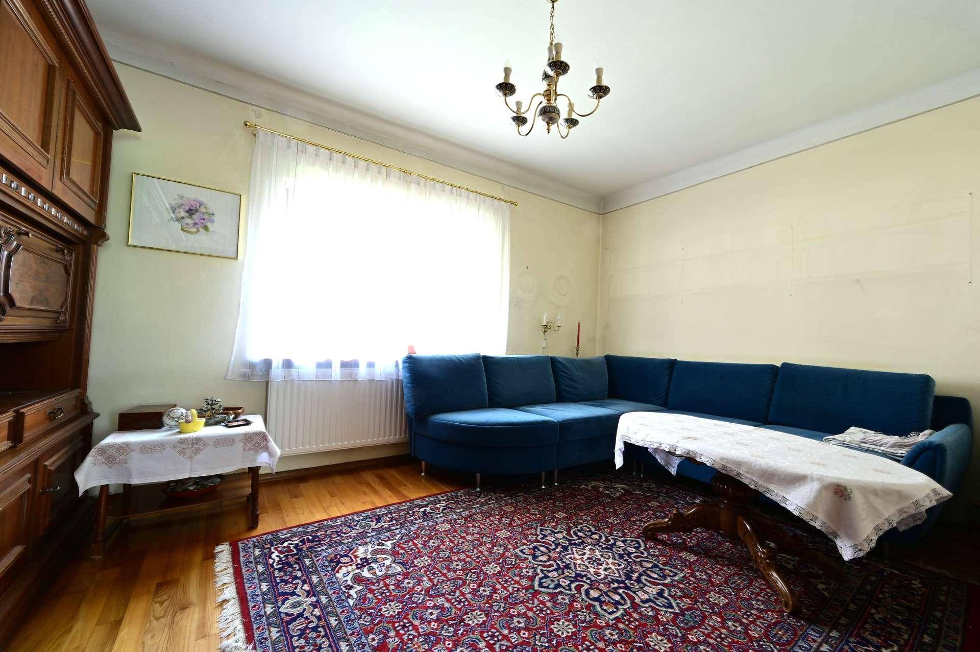 Wohnzimmer mit blauem Ecksofa, gemustertem Teppich und hellem Holzboden.