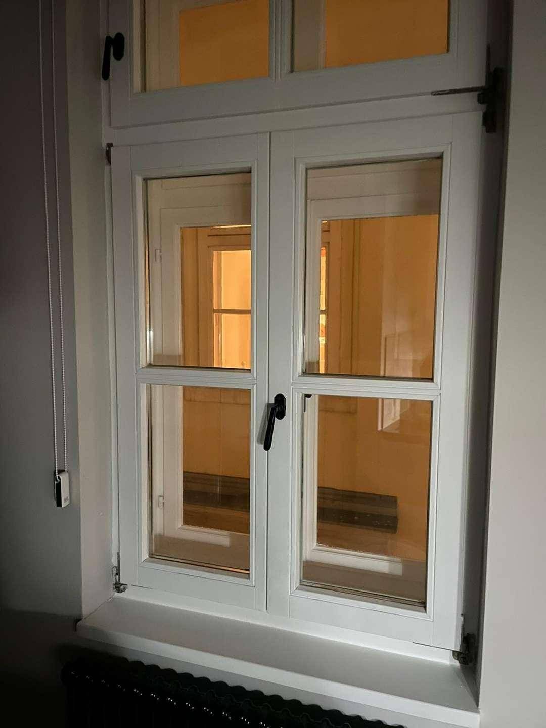 Weißes Fenster mit Doppelverglasung und Blick auf einen hell erleuchteten Innenraum.