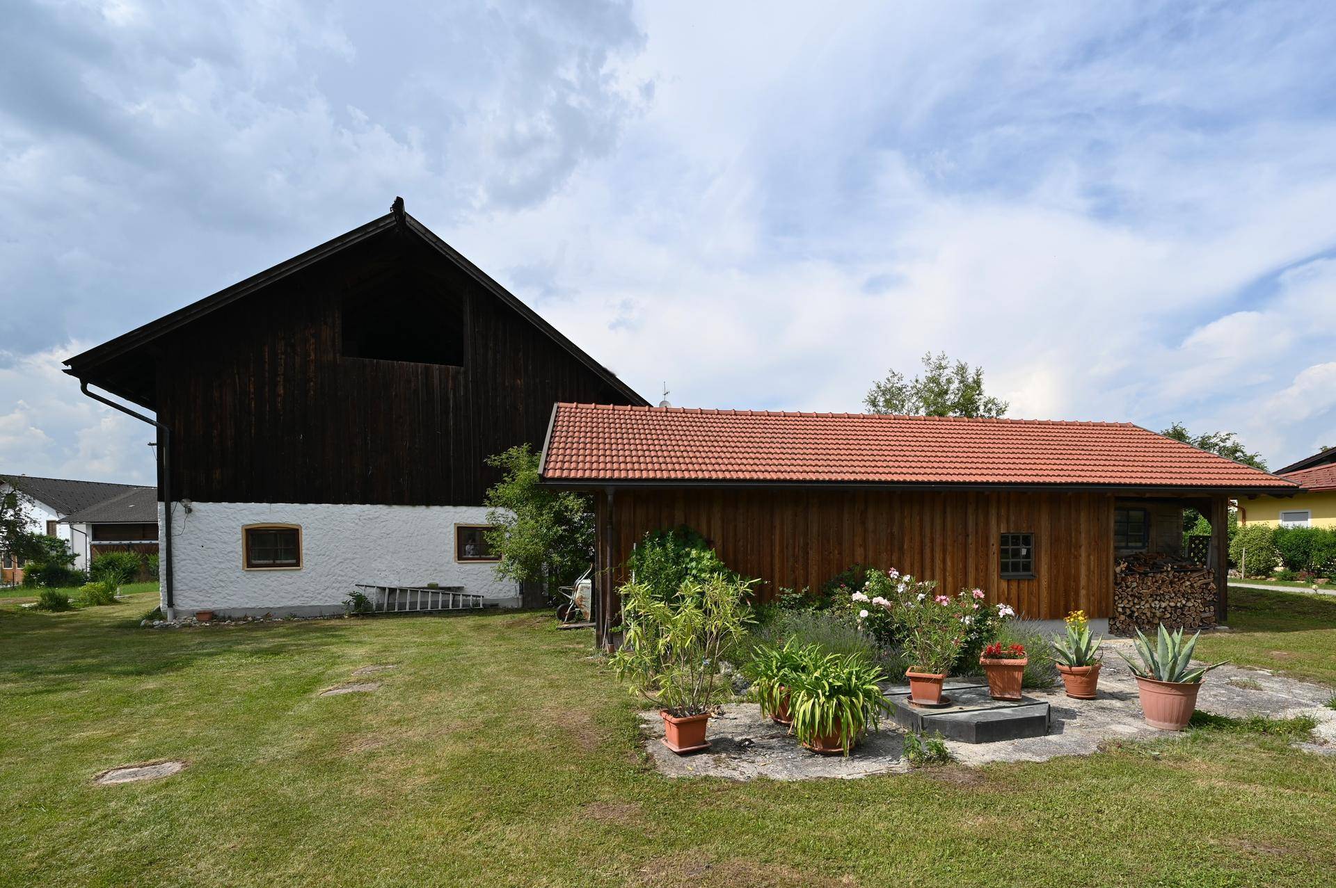 Großer Gartenbereich mit Rasenfläche, Topfpflanzen und traditionellen Holzgebäuden im Hintergrund.