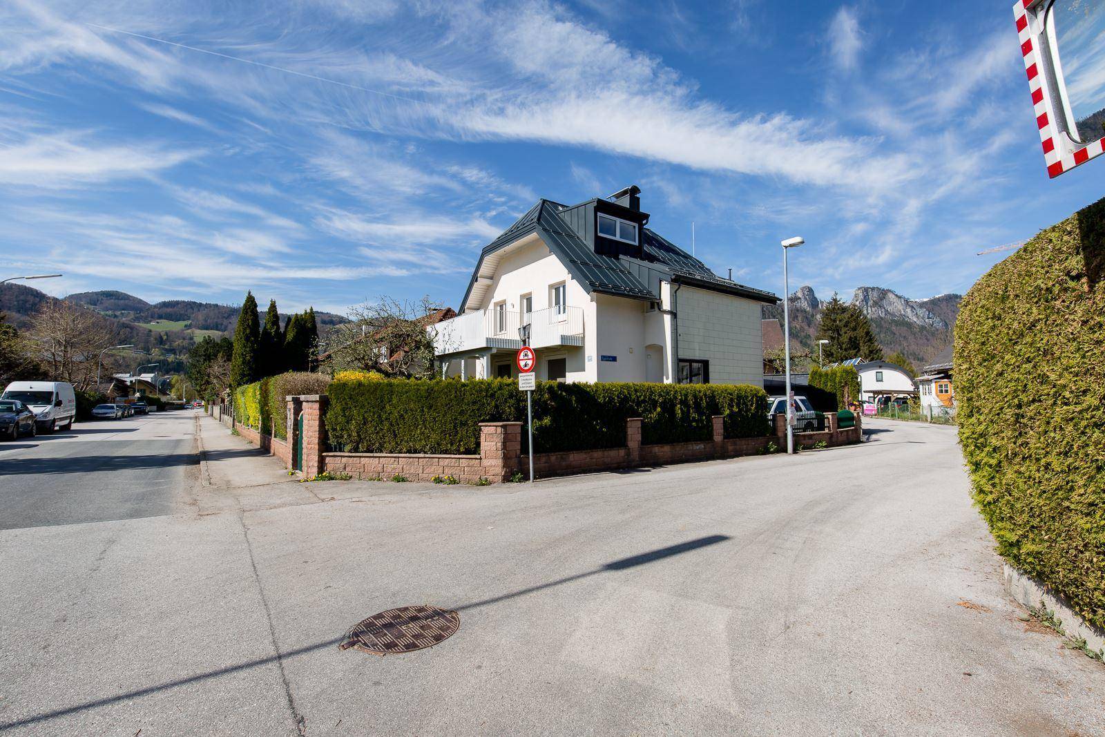 Einfamilienhaus an einer ruhigen Straße mit gepflegter Hecke und Bergblick.