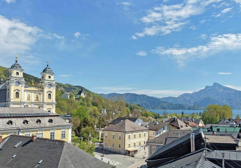 Malerischer Blick über eine Stadt mit historischer Kirche, See und majestätischen Bergen im Hintergrund.