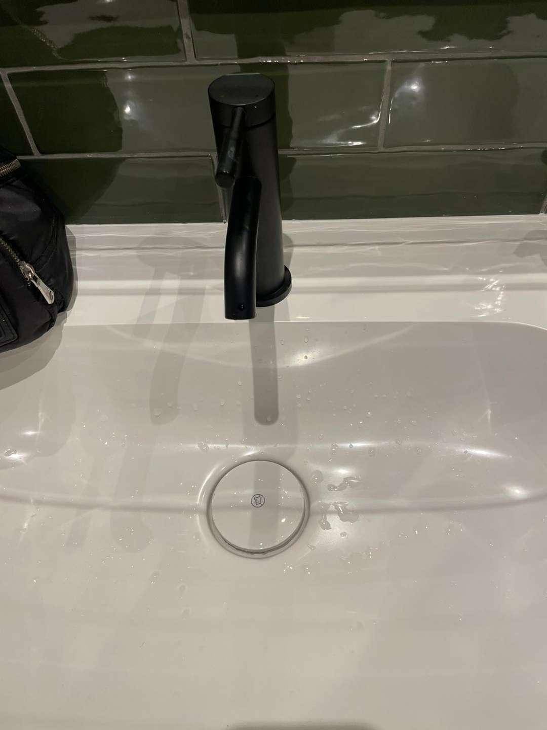 Moderner Waschtisch mit schwarzem Wasserhahn und grünen Fliesen an der Wand.