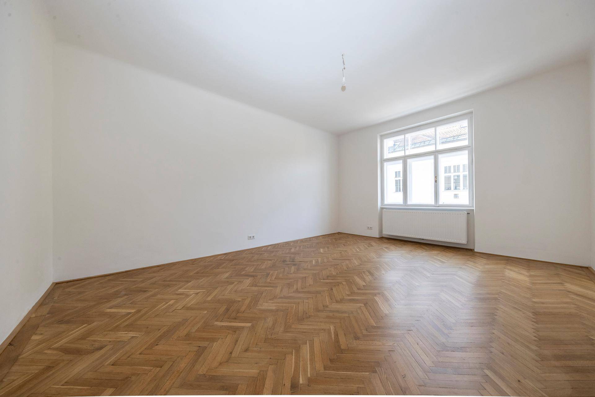 Geräumiges Zimmer mit klassischem Fischgrätparkett und einem großen Fenster für natürliche Belichtung.