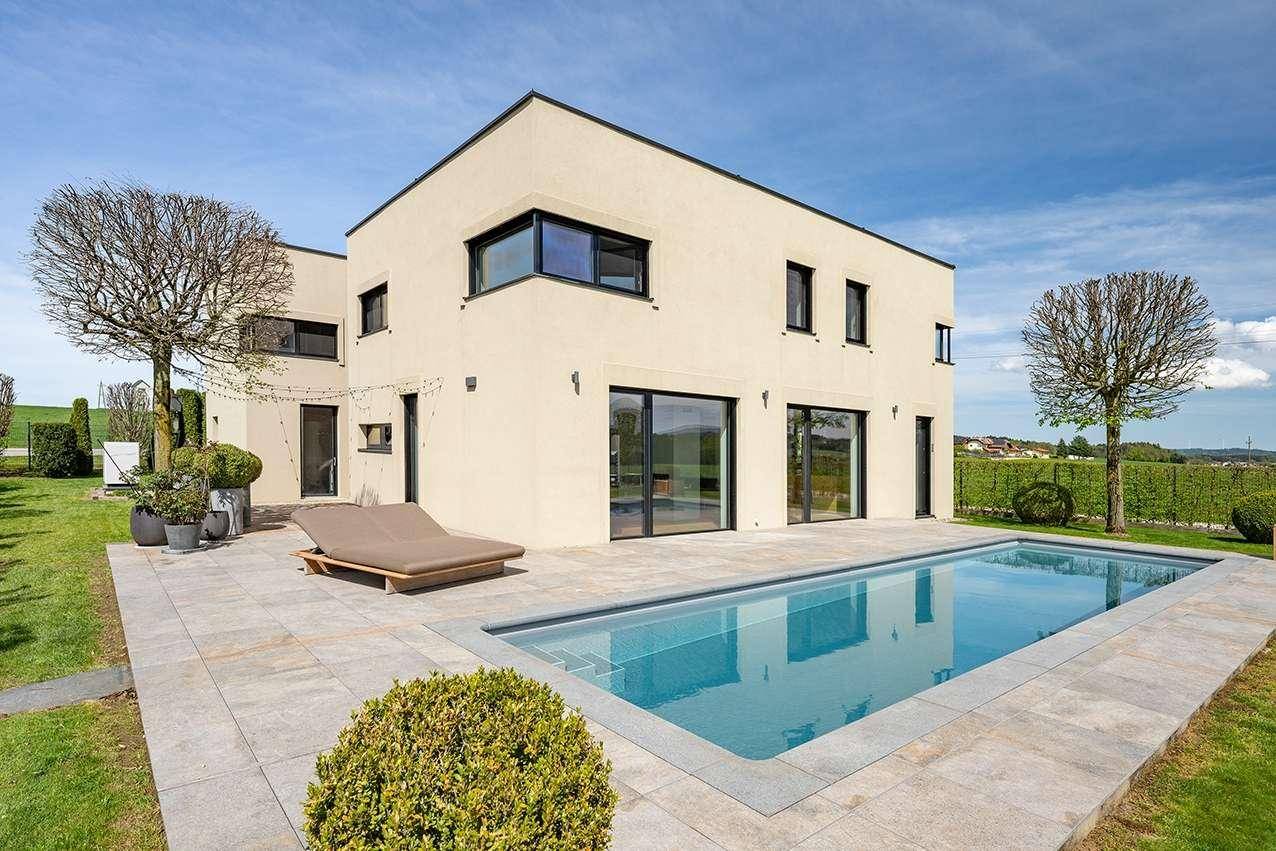Elegantes modernes Haus mit großem Poolbereich und gepflegtem Rasen unter blauem Himmel.