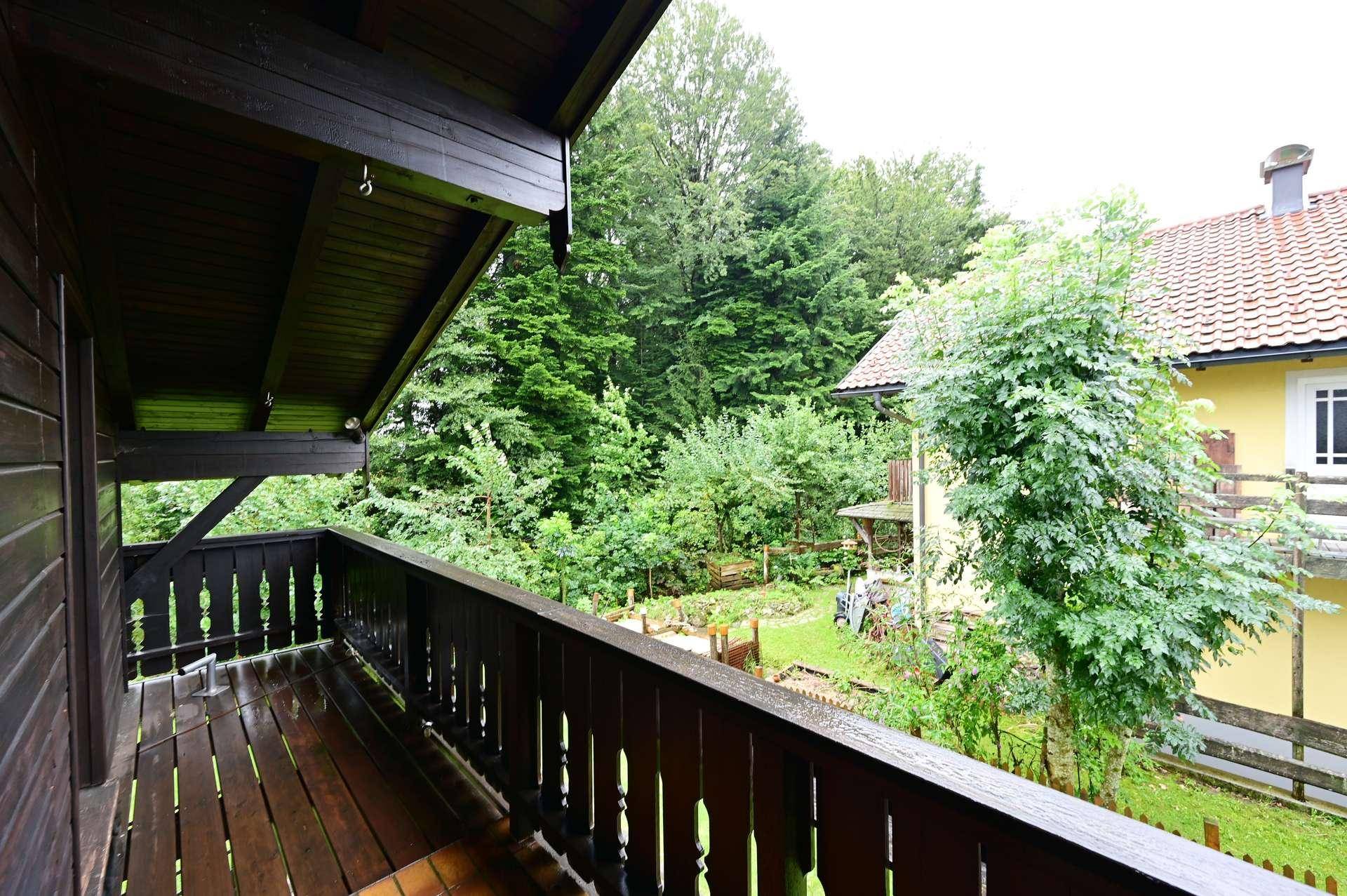 Geräumiger Holzbalkon mit Blick auf den üppigen grünen Garten und alte Bäume.