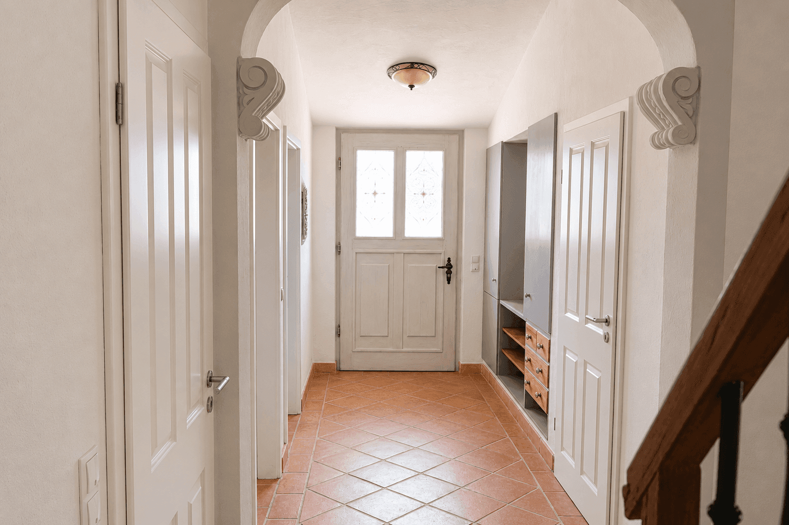 Freundlicher Eingangsbereich mit Terrakotta-Fliesen, weißer Haustür und praktischem Einbauschrank.