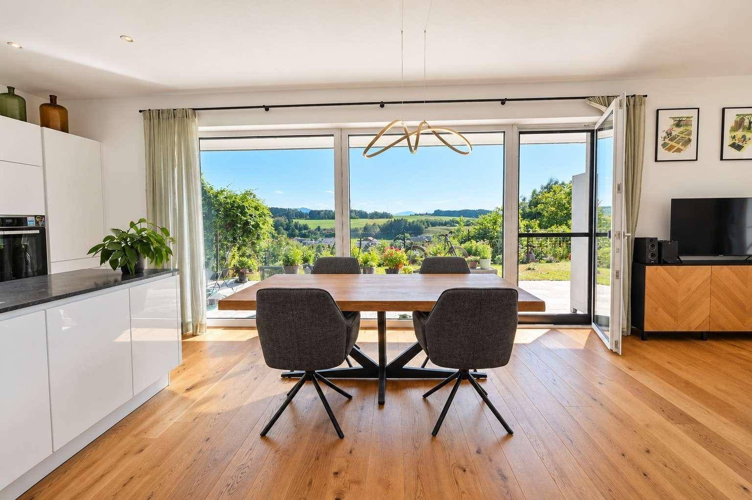 Moderner Essbereich mit Holztisch und Blick auf die grüne Landschaft durch große Fenster.