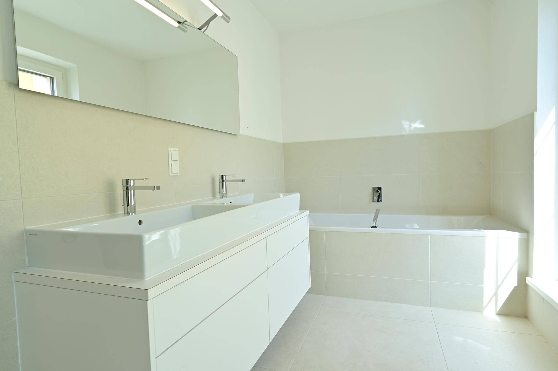 Geräumiges Badezimmer mit elegantem Doppelwaschbecken, integrierter Badewanne und hellen Fliesen.