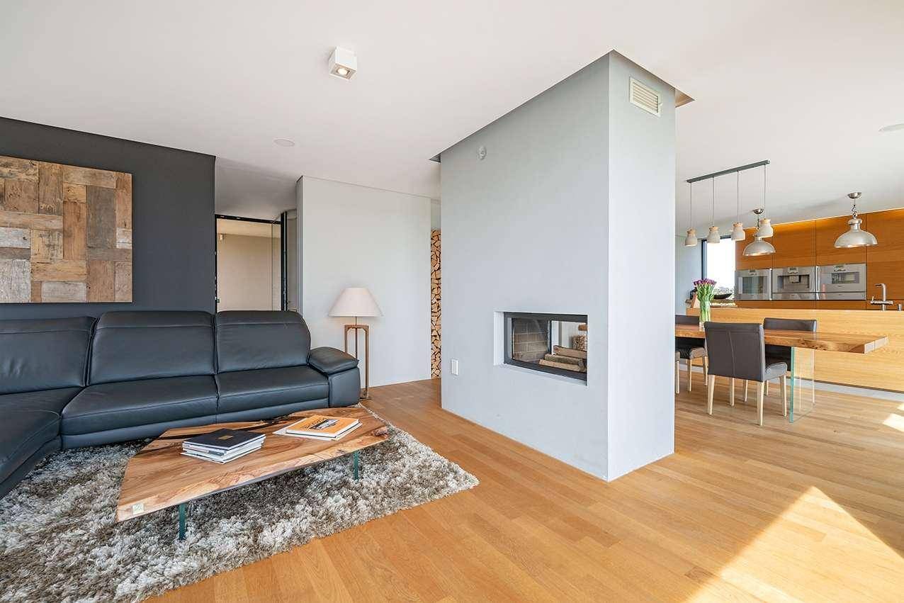 Offener Wohn- und Essbereich mit Kamin, Ledersofa und Blick auf die moderne Holzküche.