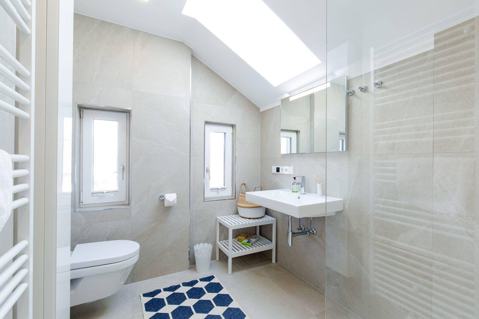Modernes Badezimmer mit Dusche, WC, Waschbecken, Dachfenster und beheiztem Handtuchhalter.