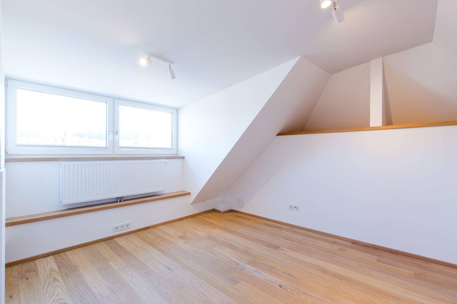 Leeres Schlafzimmer im Dachgeschoss mit Holzboden, Dachschräge und großen Fenstern.