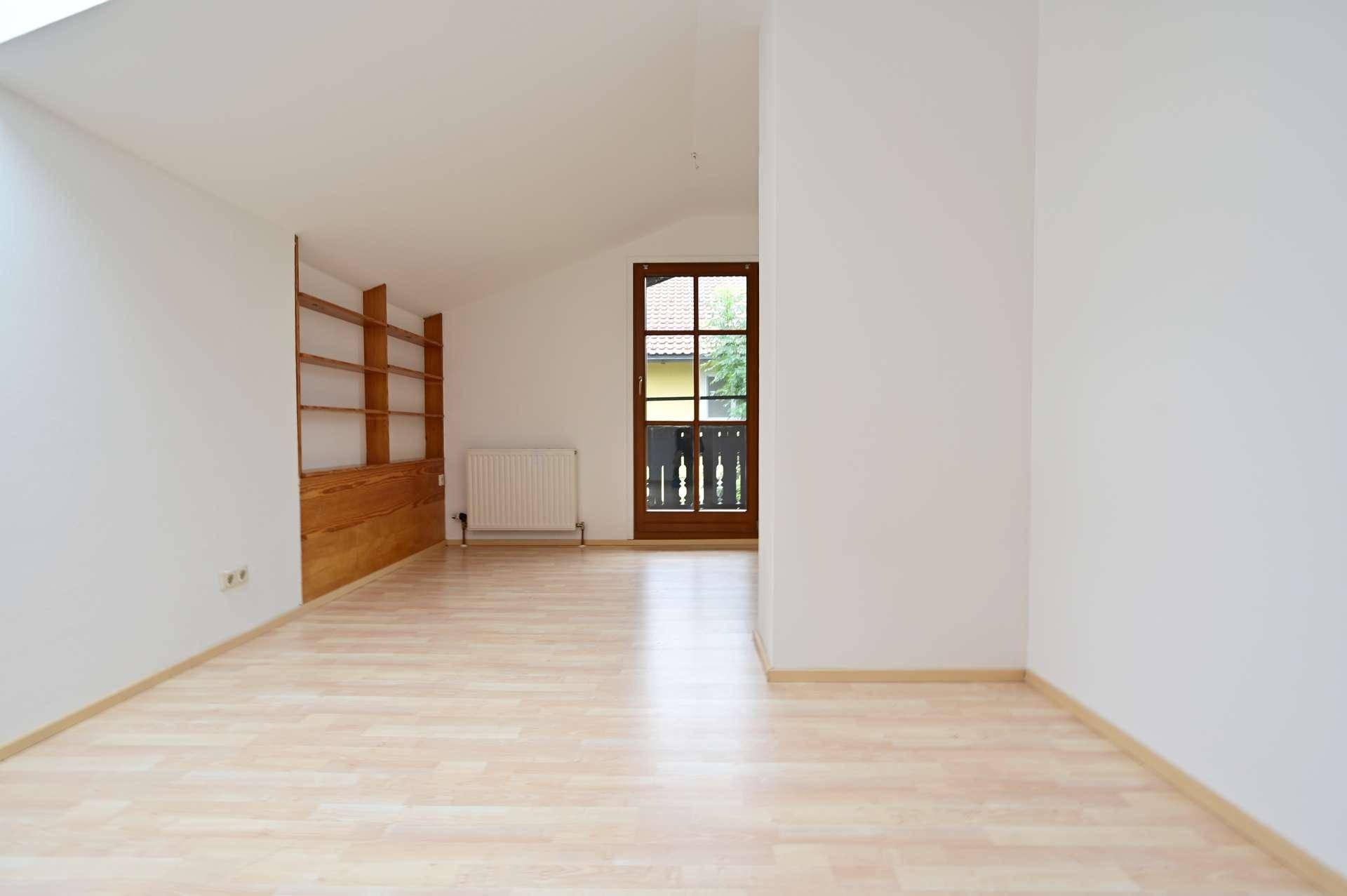 Helles Zimmer mit Laminatboden, Dachschräge und Zugang zu einem französischen Balkon.