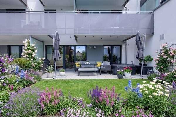 Attraktiver Gartenbereich mit großer Terrasse, Rasen und vielfältigen Blumenarrangements.