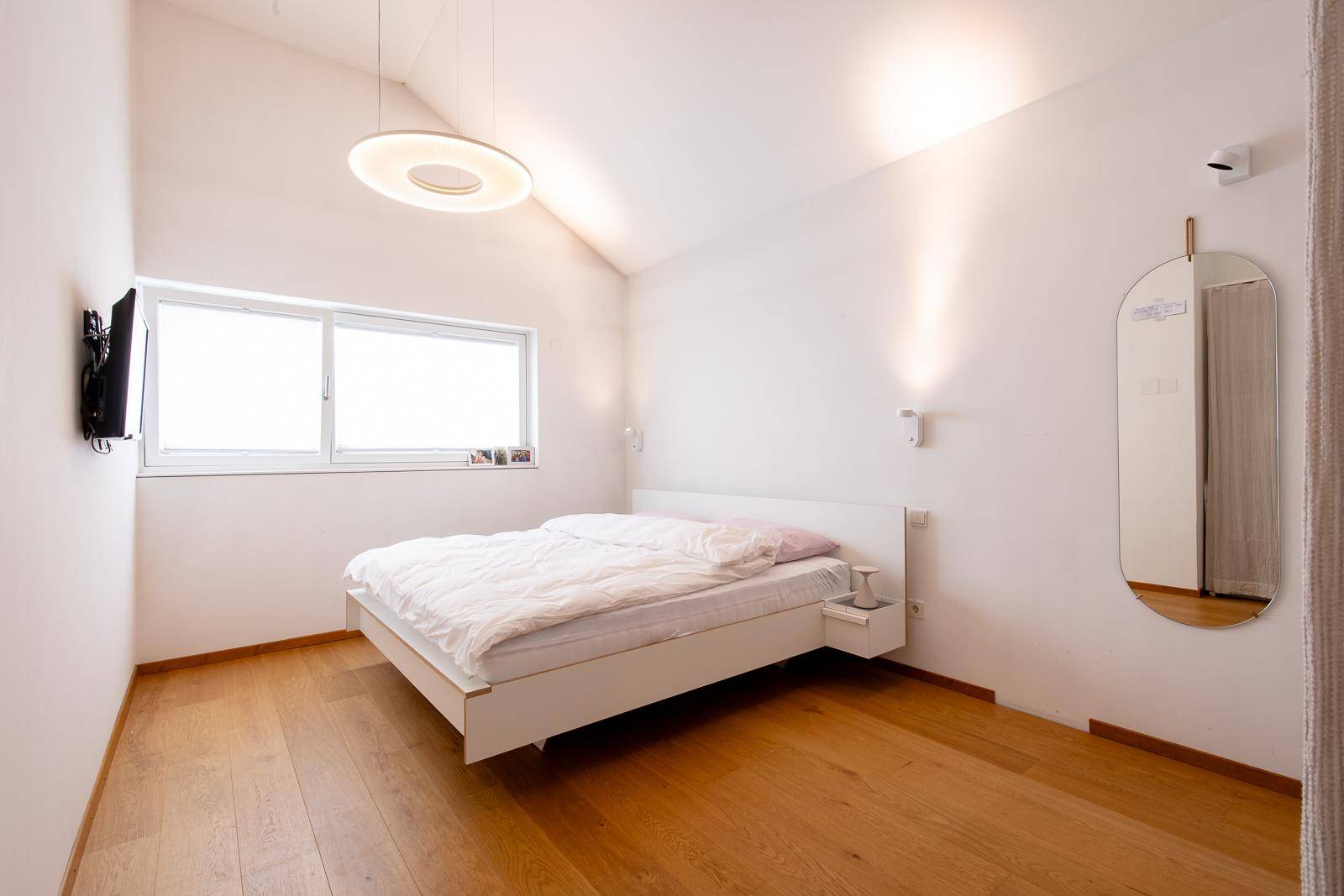 Modernes Schlafzimmer mit Holzboden, schrägen Decken und einem großen Fenster für viel Tageslicht.