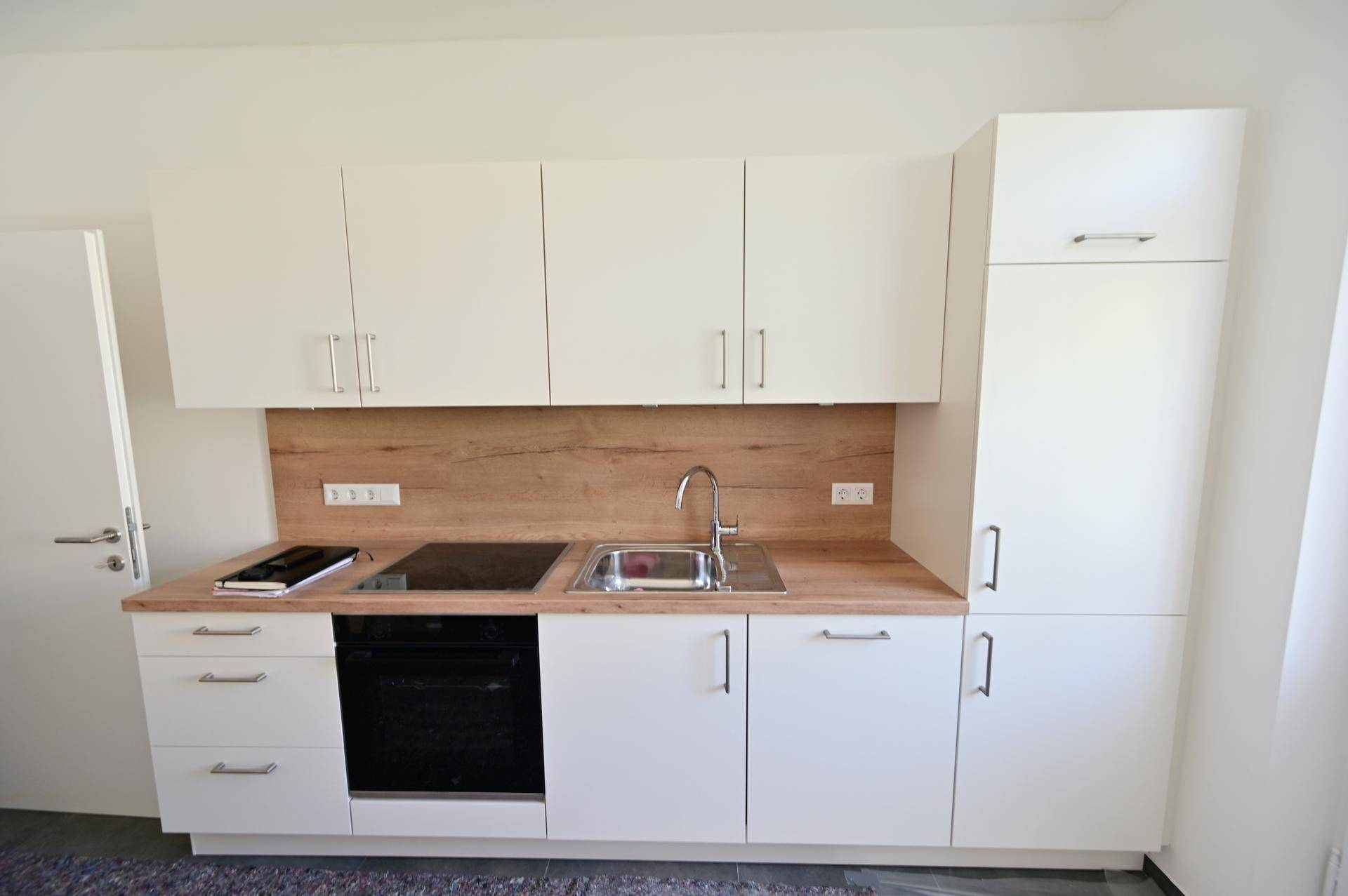 Moderne Küchenzeile mit hellen Schränken, Holz-Arbeitsplatte und integrierten Elektrogeräten.