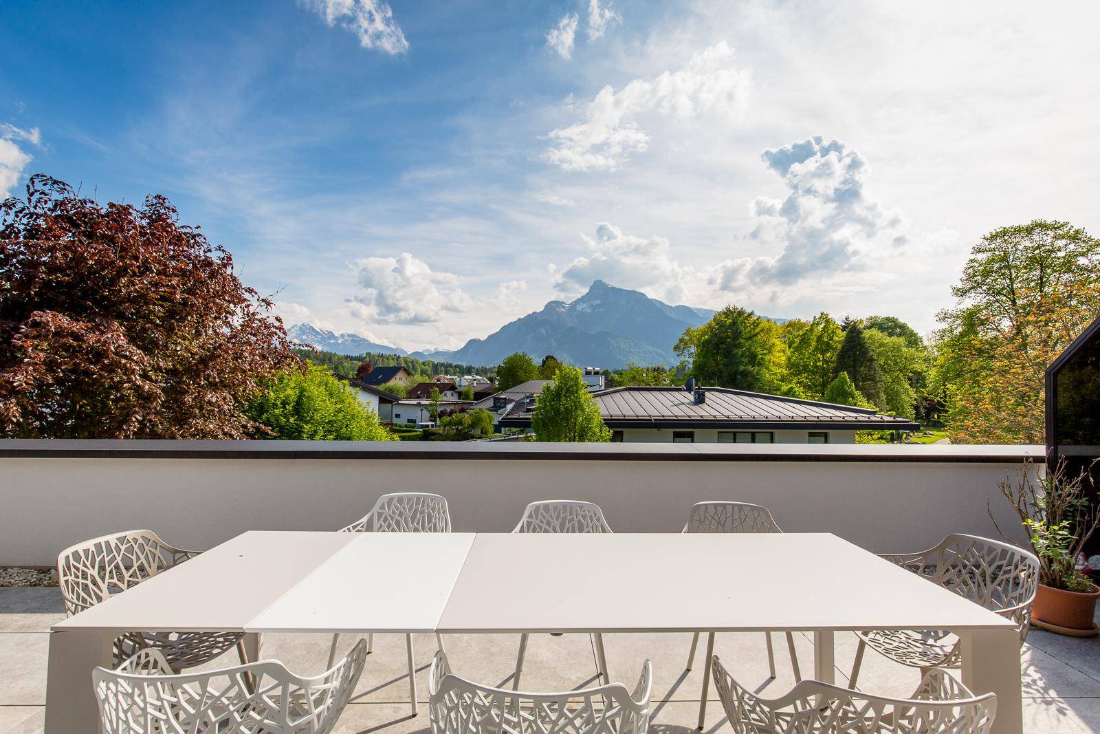 Große Dachterrasse mit Esstisch, modernen Stühlen und weitem Bergblick unter blauem Himmel.