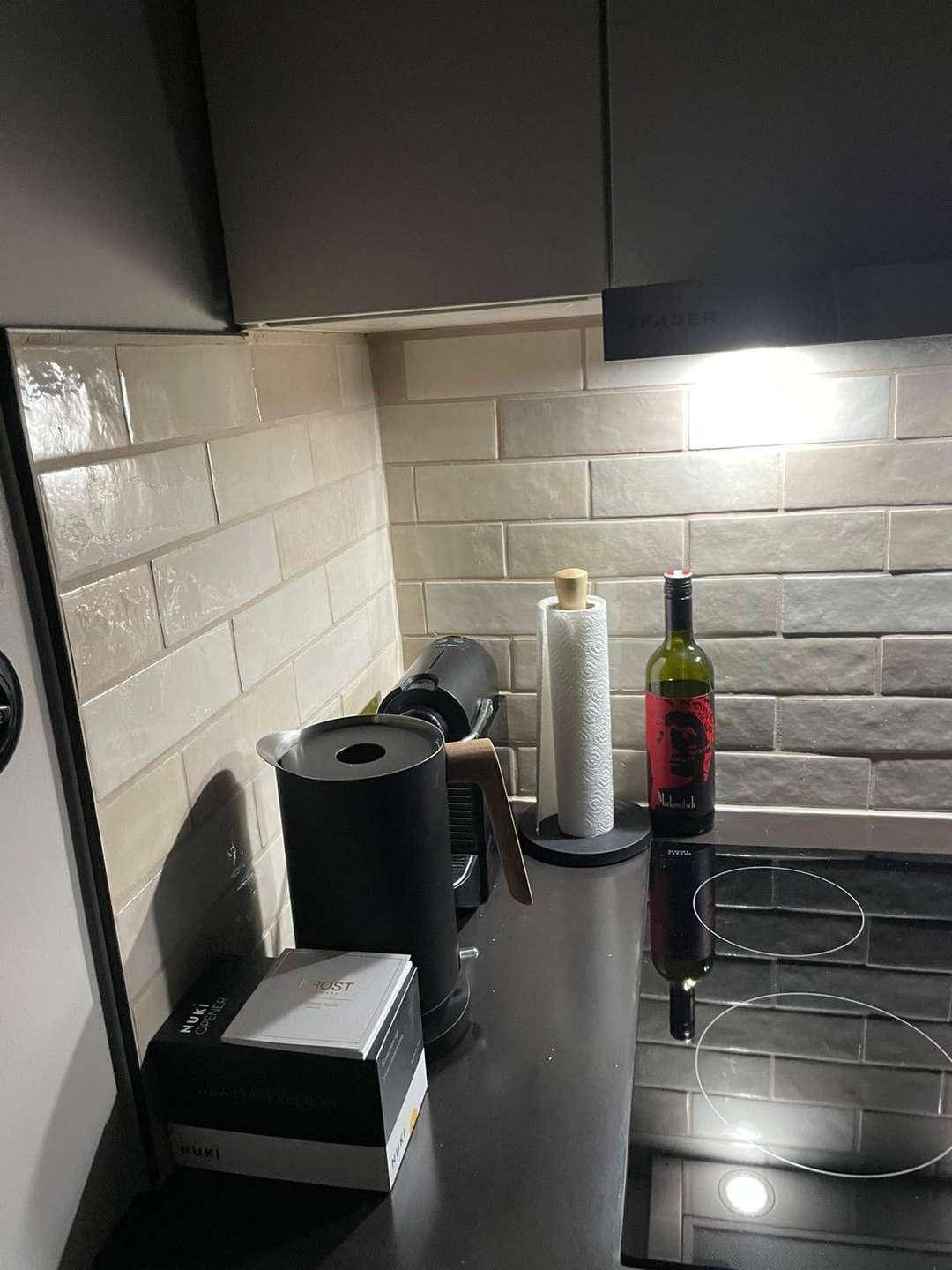 Moderne Küchenzeile mit Induktionskochfeld, Kaffeemaschine und hellen Fliesen.