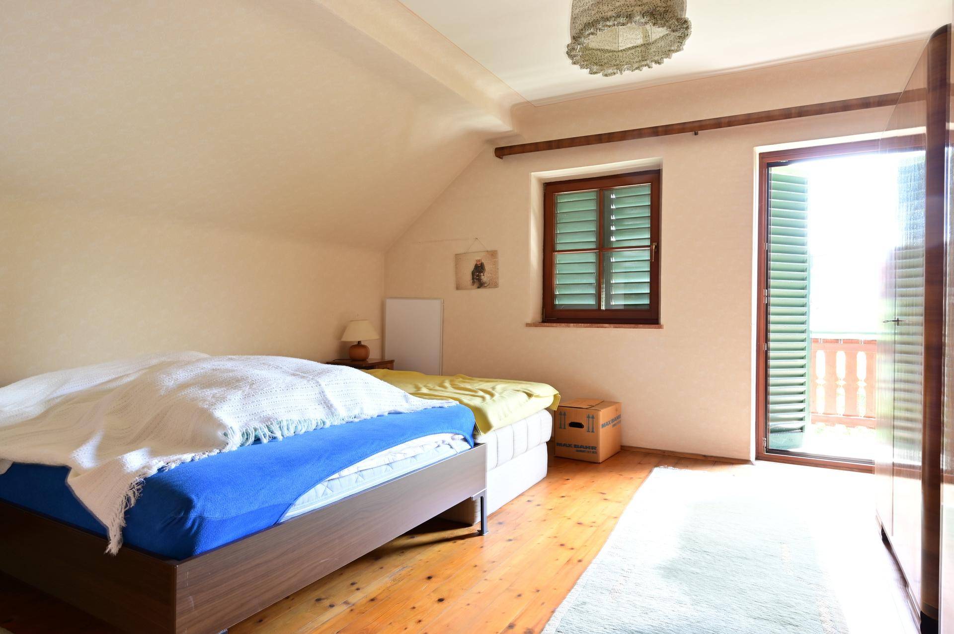 Helles Schlafzimmer im Dachgeschoss mit Holzboden, Fensterläden und Balkonzugang.