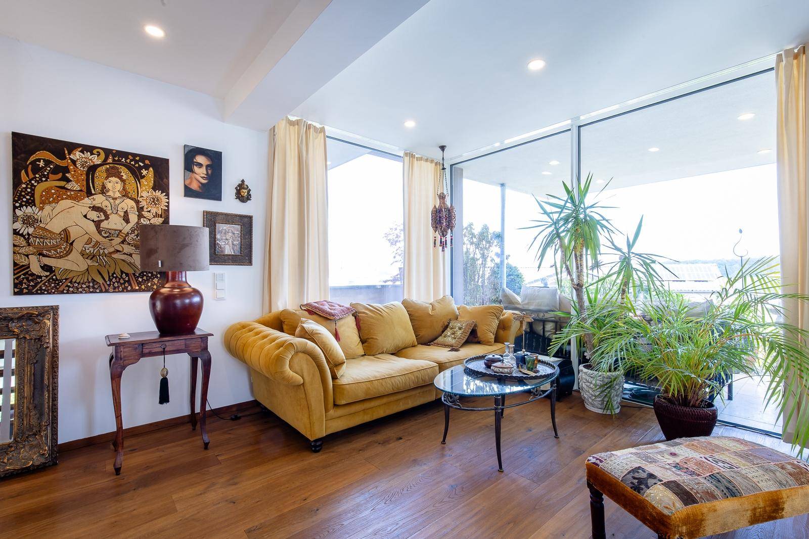 Stilvolles Wohnzimmer mit gelbem Sofa, Holzboden und großen Fensterfronten mit viel Tageslicht.
