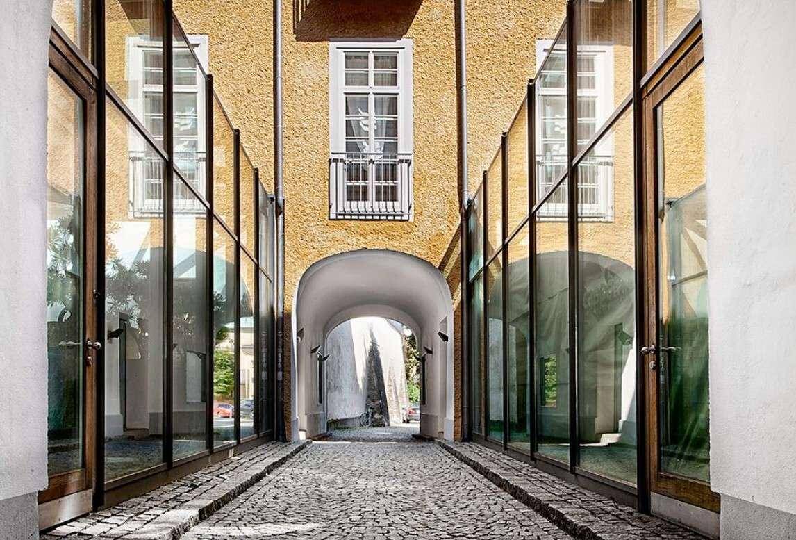 Historischer Durchgang mit Kopfsteinpflaster, umgeben von modernen Glasfassaden und einem französischen Balkon.