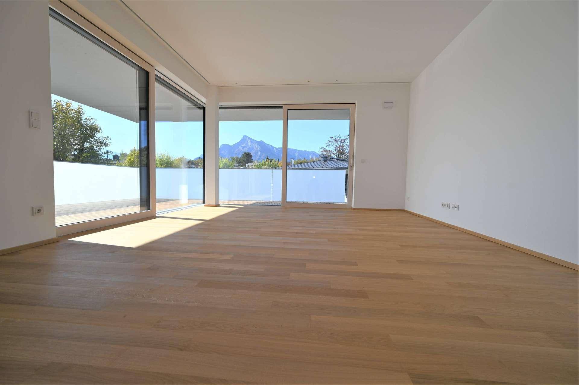 Heller, leerer Wohnraum mit Eichenparkett und großen Fenstern, die einen beeindruckenden Bergblick bieten.