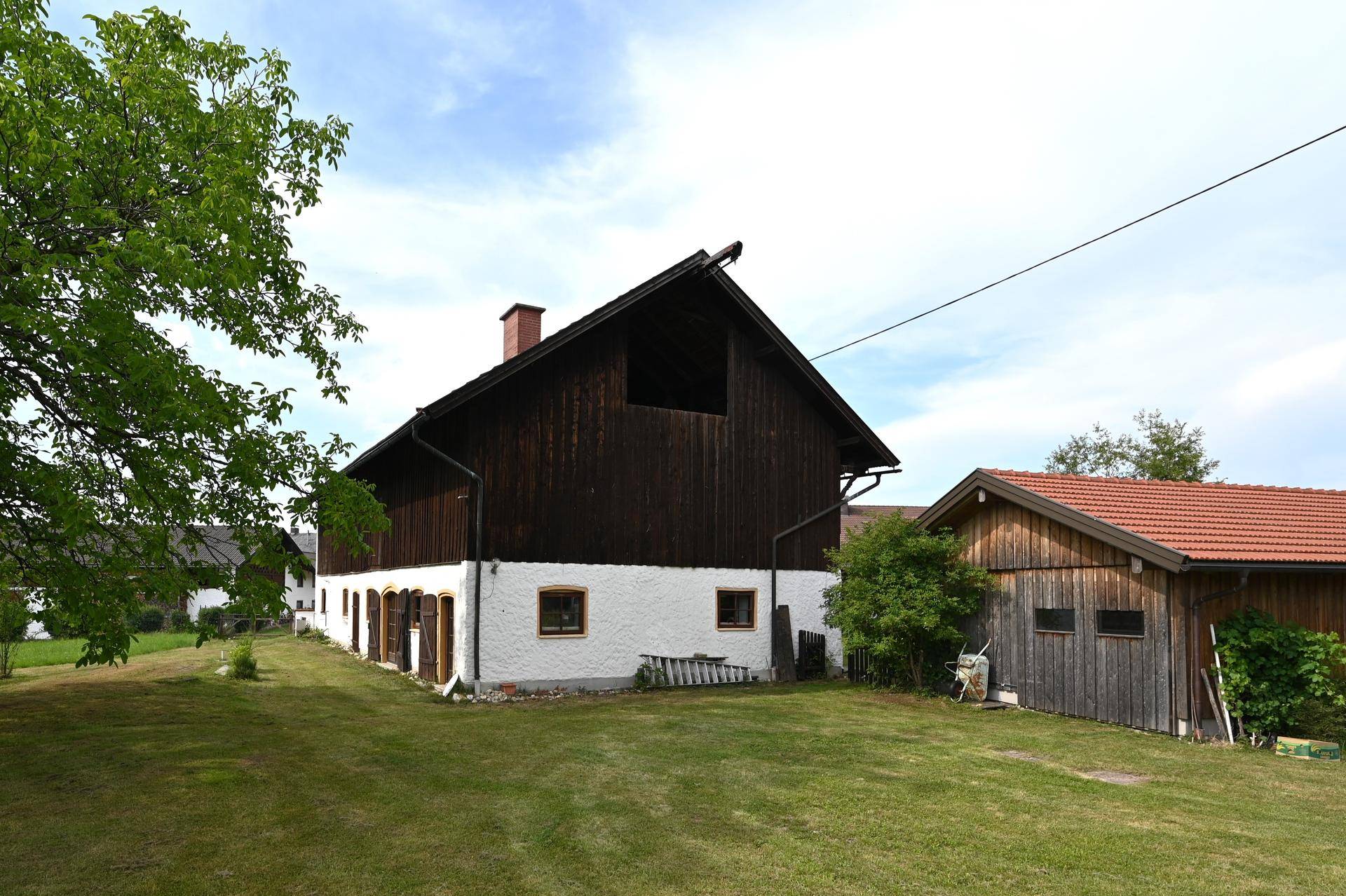 Ländliches Anwesen mit traditioneller Holzscheune und einem kleinen Nebengebäude auf einer grünen Wiese.