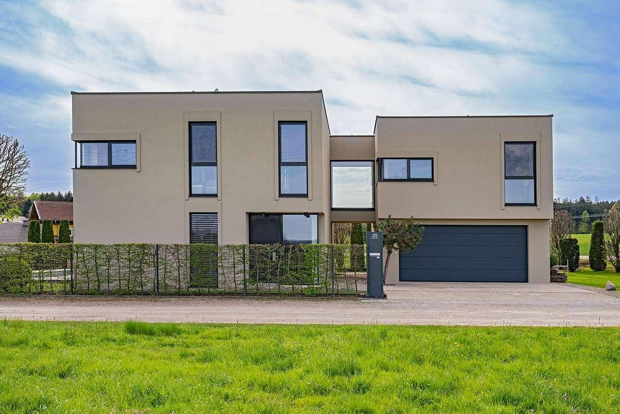 Moderne Hausfassade mit integrierter Garage, gepflegter Hecke und breiter Zufahrt.