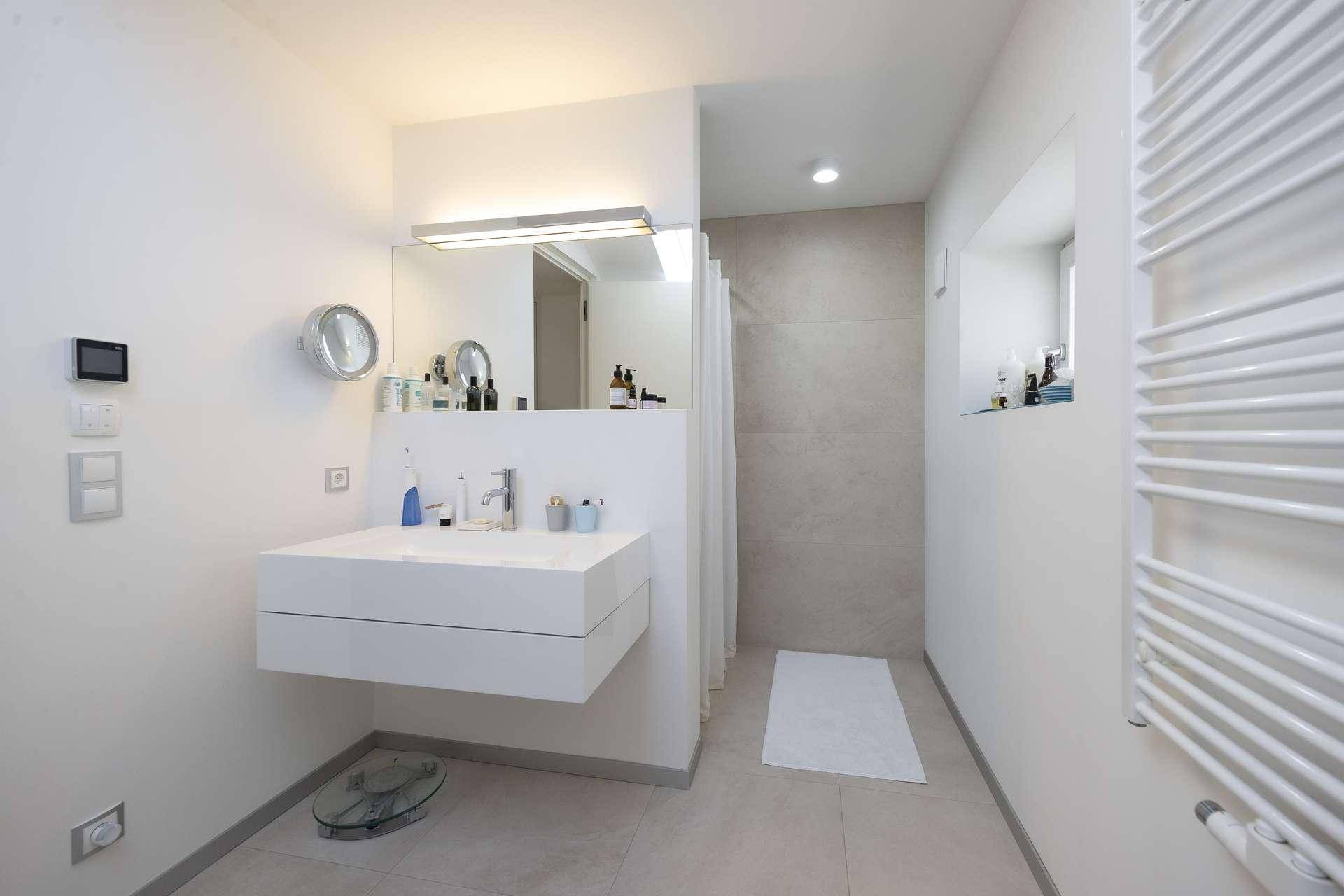 Modernes Badezimmer mit schwebendem Waschbecken, großer Spiegelfläche und Handtuchheizkörper.