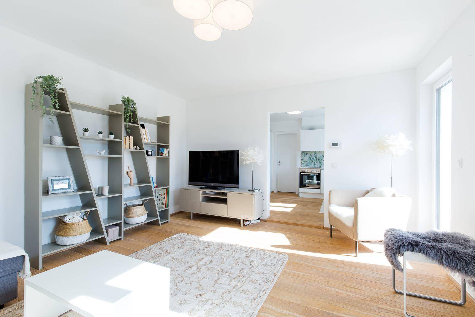 Helles Wohnzimmer mit Holzboden, TV-Möbel und Blick in den angrenzenden Küchenbereich.