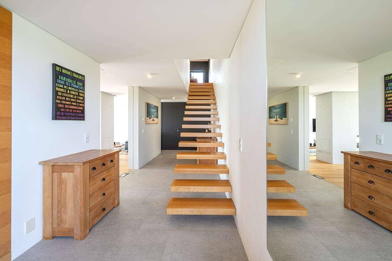 Heller Flur mit moderner schwebender Holztreppe und eleganten Holzkommoden.