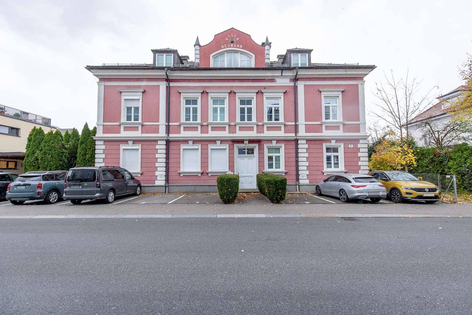 Historisches Wohngebäude mit rosa Fassade, weißen Akzenten und Parkplätzen.