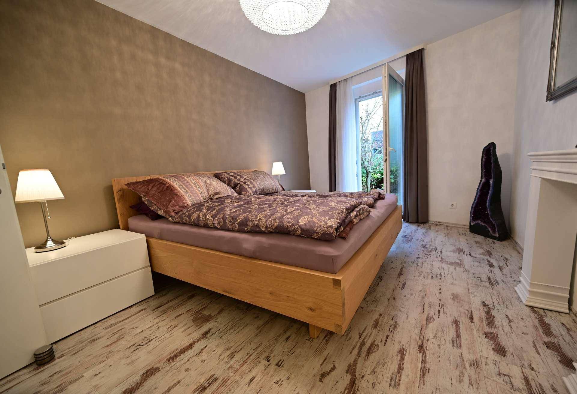 Schlafzimmer mit Holzbett, Nachttischen und Zugang zu einem Außenbereich.