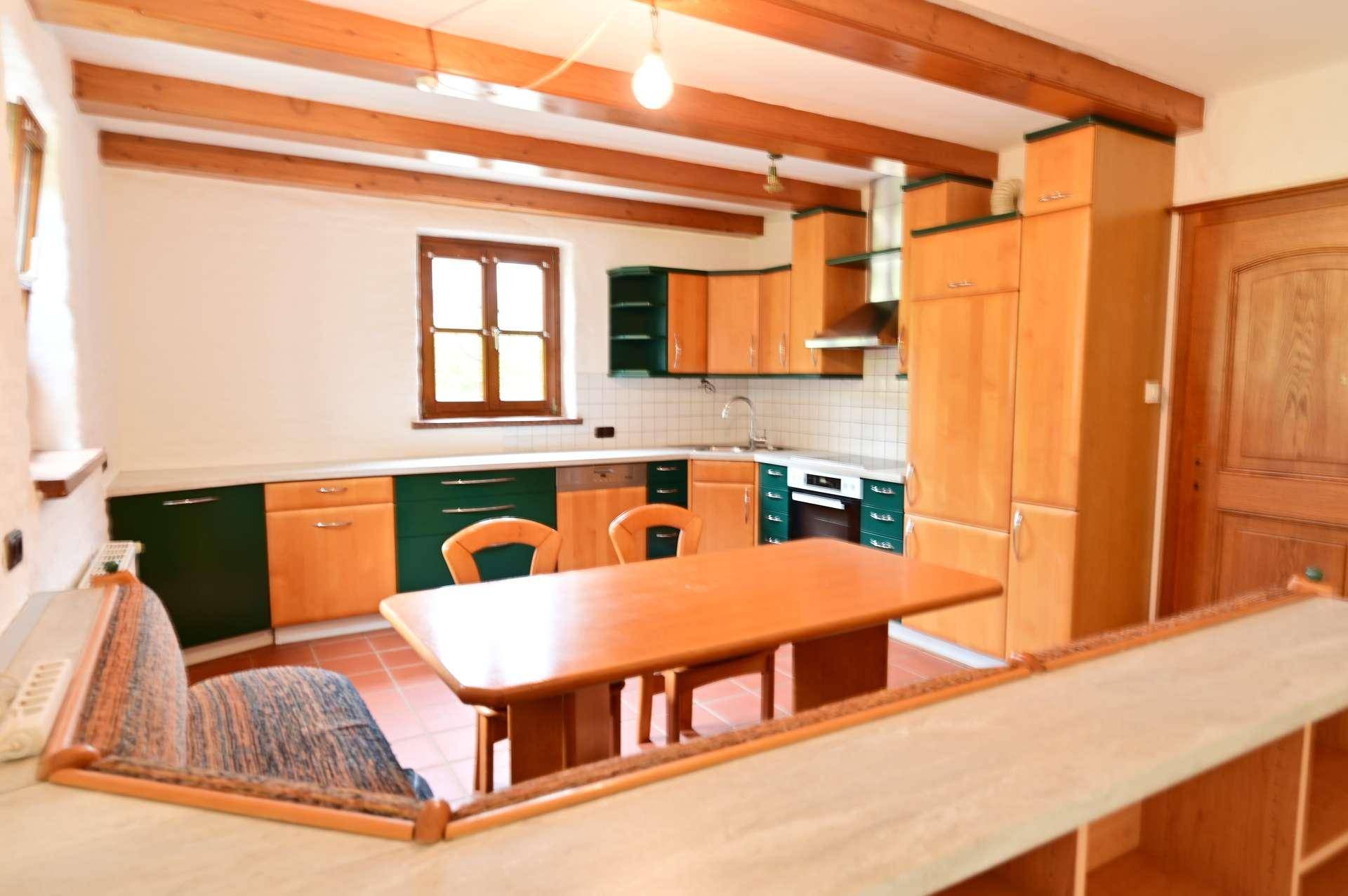 Rustikale Küche mit Holzbalkendecke, Essbereich und grünen Akzenten an den Schränken.