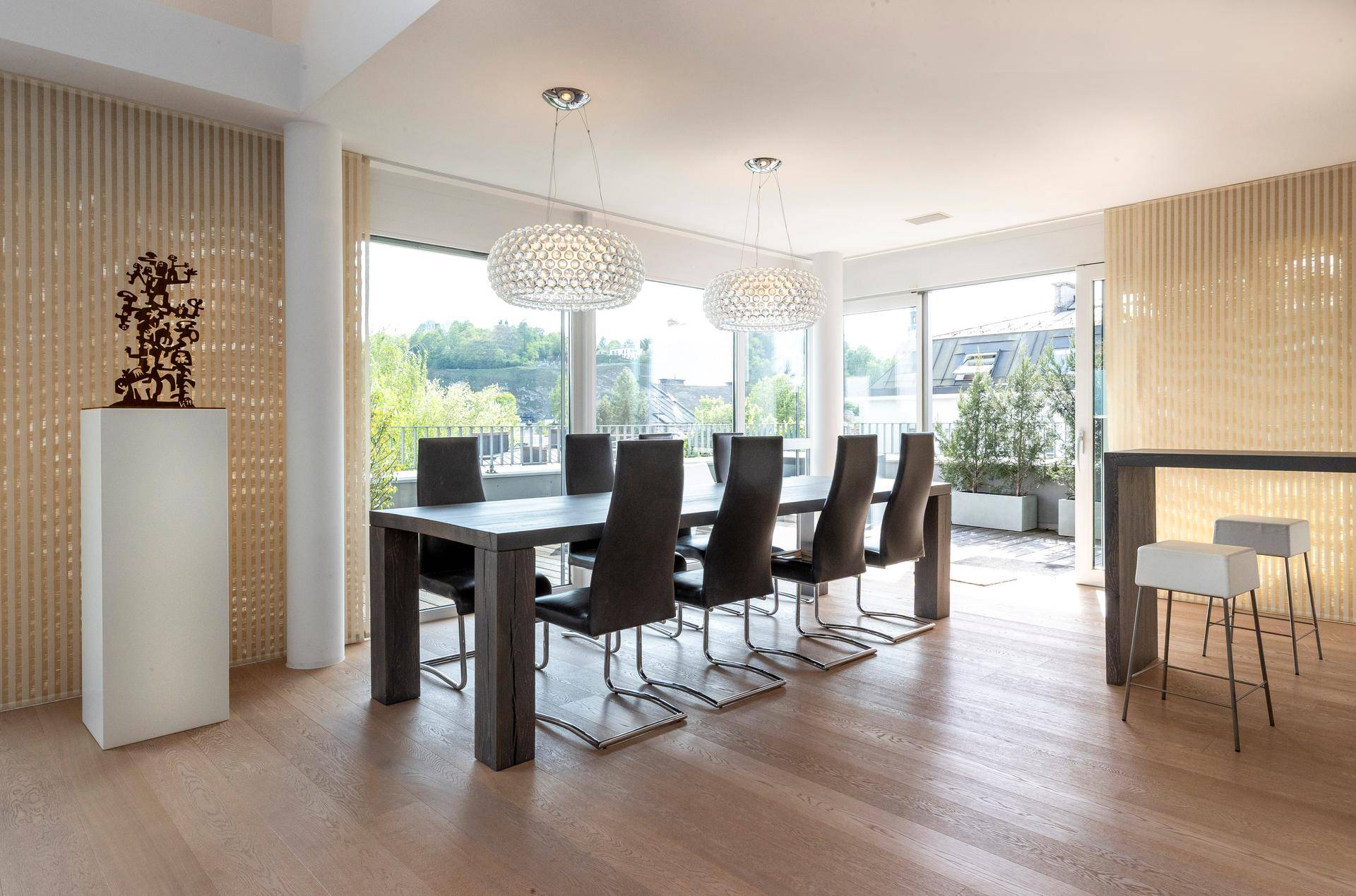Eleganter Essbereich mit großem Holztisch, modernen Leuchten und Zugang zur Terrasse.