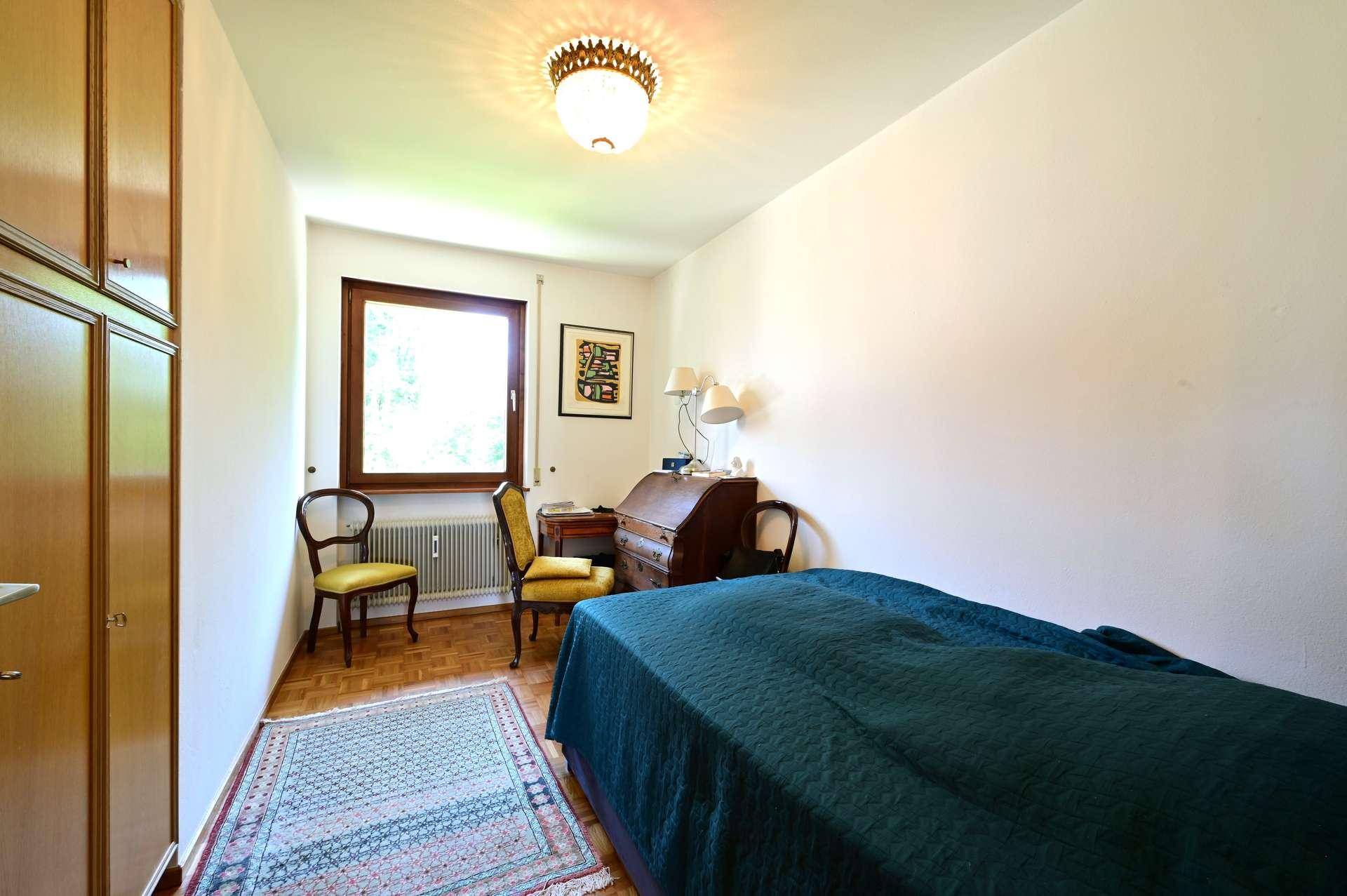 Helles Schlafzimmer mit Einzelbett, Holzschrank, Schreibtisch und einem Fenster.