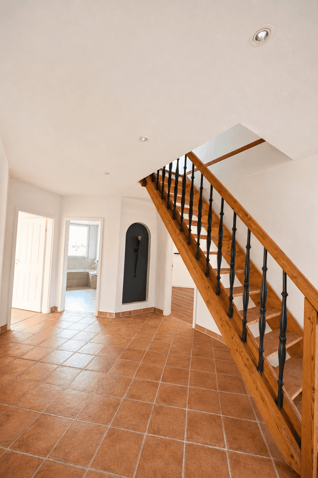 Geräumiger Eingangsbereich mit Terrakotta-Fliesenboden und einer eleganten Holztreppe.