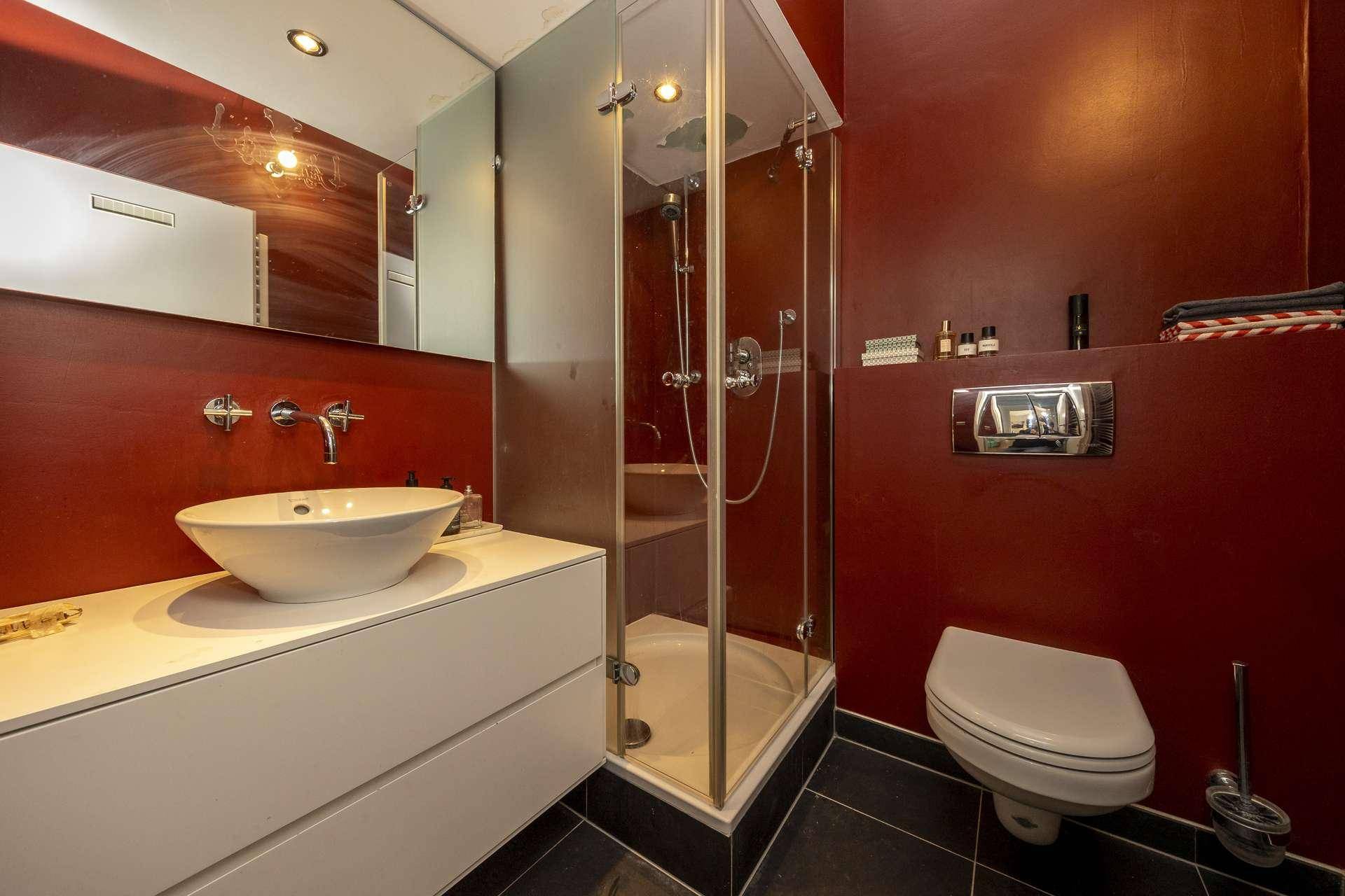 Modernes Badezimmer mit begehbarer Dusche, Waschbecken und Wand-WC, in Rot und Weiß gehalten.